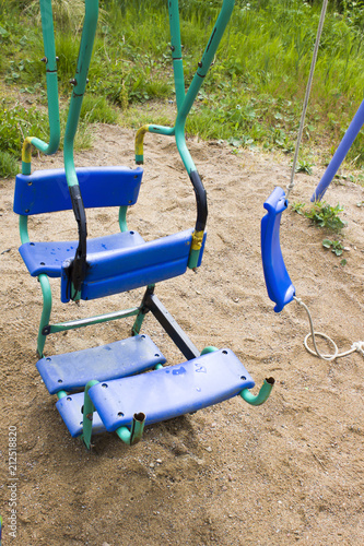 Broken plastic children's swing in a playground, painted, welding on metal, so as not to break, old and unsafe swings. Summer, under the swing of sand. The concept of child safety in games, game