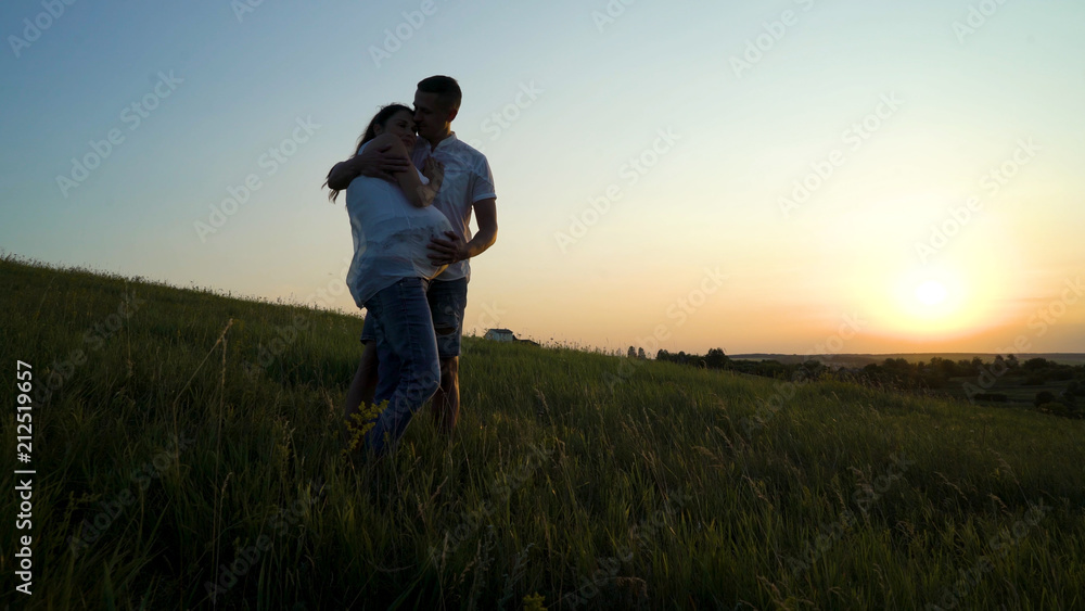 Romantic young happy pregnant couple hugging in nature at sunset. Man hugging woman from back in the evening in fields. Family, marriage, love, devotion, faith concept Romantic young happy pregnant couple hugging in nature at sunset. Man hugging woman from back in the evening in fields. Family, marriage, love, devotion, faith concept