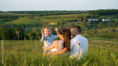 Pregnant couple with toddler daughter have leisure time outdoors back view. Happy young parents expecting baby with child at sunset. Parenthood, pregnancy, childhood, healthy, activity concept