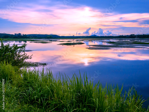 Fototapeta Naklejka Na Ścianę i Meble -  sunrise over big lake with reflection and green grass in foreground at Trad Thailand