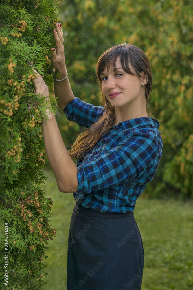 Landscape designer. Smiling beautiful brunette woman posing on green thuja trees background Landscape designer. Smiling beautiful brunette woman posing on green thuja trees background