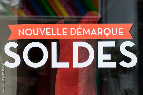 discount sign "SOLDES nouvelle demarque" in french, the traduction of (sales, new markdown) on window in french fashion store showroom on summer clothes background