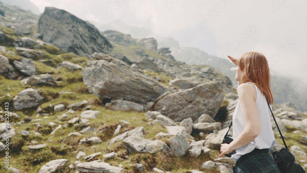 A young woman hiker walks in the mountains with photo camera. Transfagarasan, Carpathian mountains in Romania A young woman hiker walks in the mountains with photo camera. Transfagarasan, Carpathian mountains in Romania