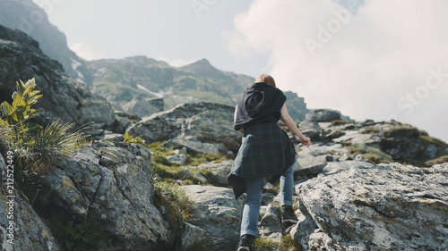 A young woman hiker walks in the mountains with photo camera. Transfagarasan, Carpathian mountains in Romania © tol_u4f
