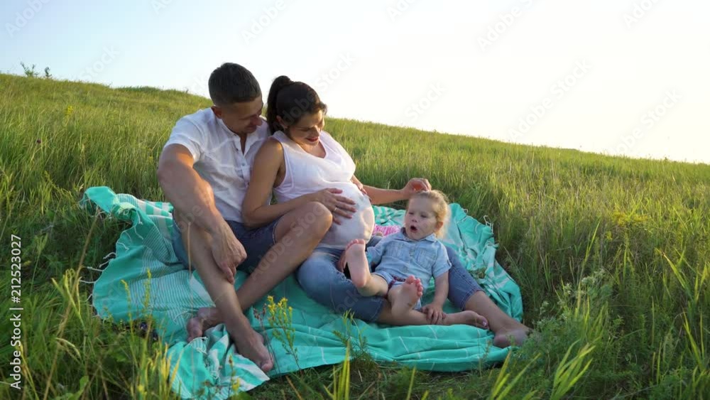 Pregnant couple with toddler daughter have leisure time outdoors on blanket. Happy young parents expecting baby with child at sunset. Parenthood, pregnancy, childhood, healthy, activity concept Pregnant couple with toddler daughter have leisure time outdoors on blanket. Happy young parents expecting baby with child at sunset. Parenthood, pregnancy, childhood, healthy, activity concept