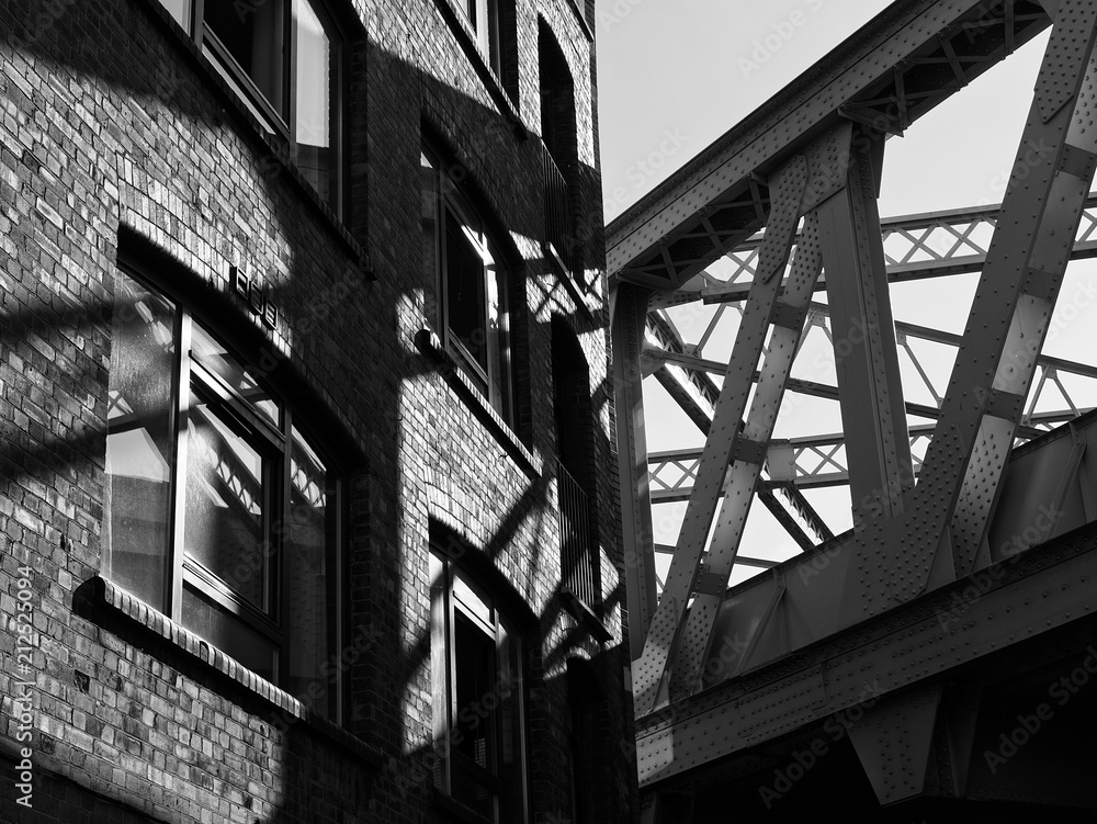 Black and white image of urban city street corner with vintage train bridge and brick wall building in London, UK