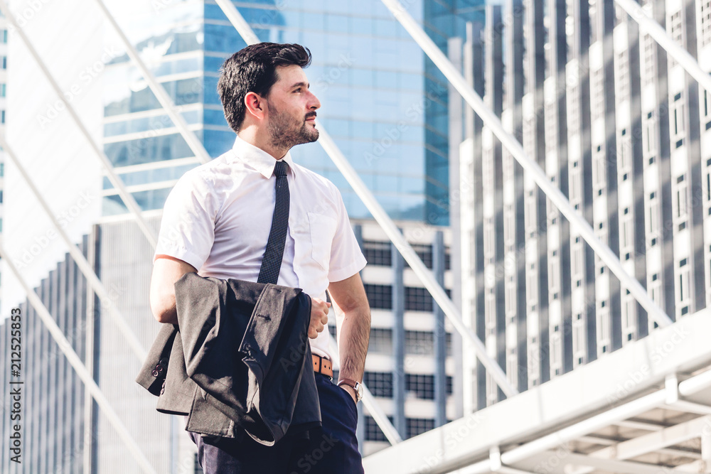 Portrait of handsome businessman in black suit standing outdoors on modern city background