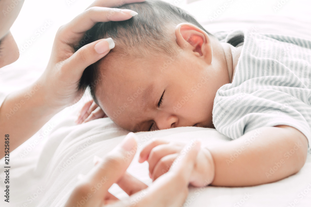 Mother holding sleeping baby hand on white bed.Love of family concept Mother holding sleeping baby hand on white bed.Love of family concept