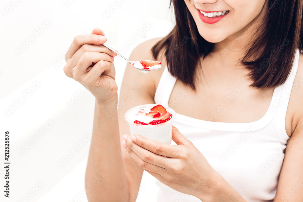 Woman eating yogurt with fresh strawberry while relaxing on sofa at home.dieting concept.healthy lifestyle