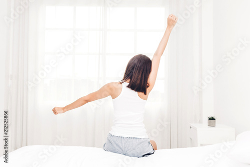 Woman sitting near the window and stretching in bed after wake up.Woman happy and relaxed breathing fresh air at morning