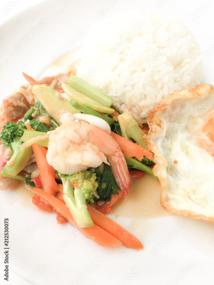 Fried Savory sauteed mixed vegetables with shimp and fried egg served with rice in white dish on white background as Thai homemade meal or recipe in the restaurant. Thai style food. Fried Savory sauteed mixed vegetables with shimp and fried egg served with rice in white dish on white background as Thai homemade meal or recipe in the restaurant. Thai style food.