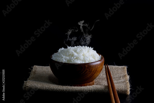Cooked rice in a wooden bowl with smoke, put on sackcloth background black.