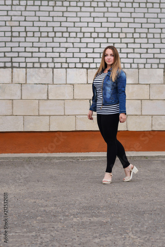 Young attractive girl in jeans jacket and striped T-shirt posing outdoors.