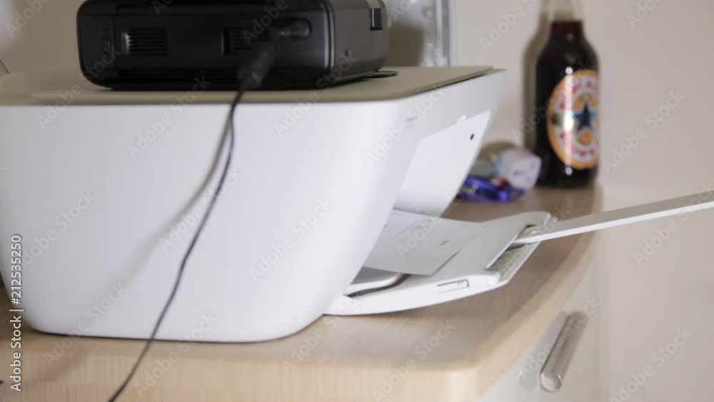 A white printer printing out a document on plain white paper, viewed from the side. A white printer printing out a document on plain white paper, viewed from the side.