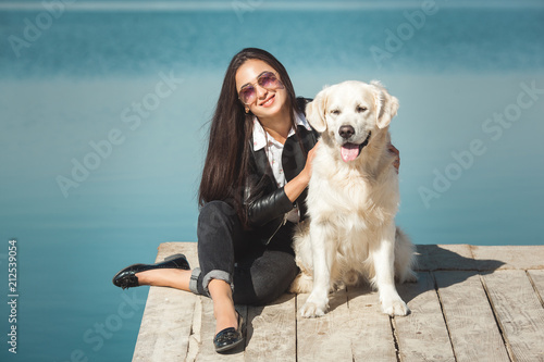 Young attractive woman sitting at the pier with her dog. Best friends outdoors