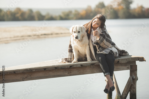 Young attractive woman sitting at the pier with her dog. Best friends outdoors