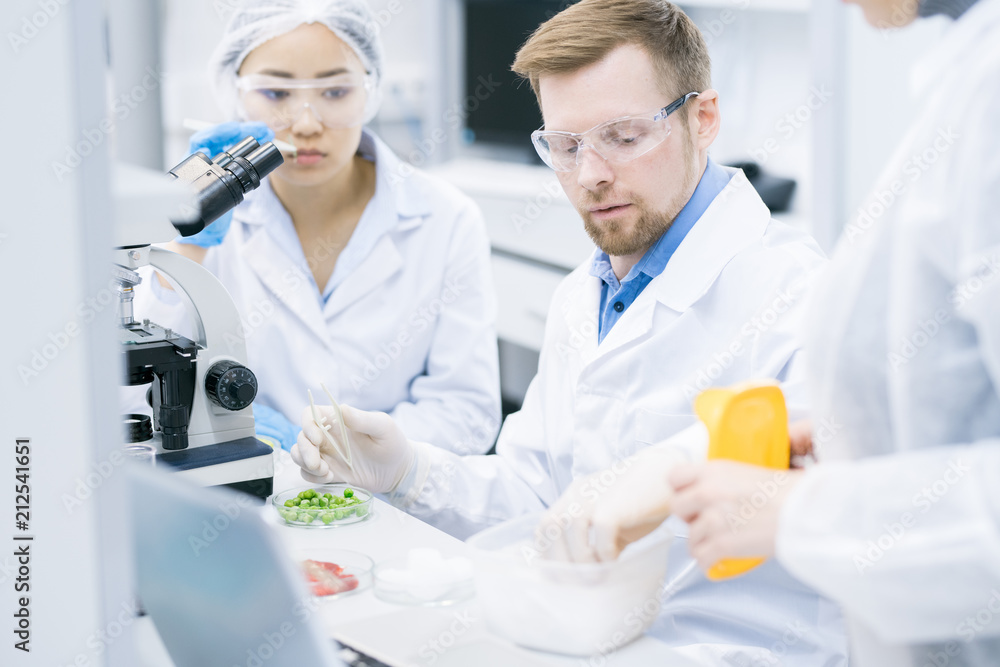 Portrait of three scientists doing research studying substances in modern laboratory, focus on young man wearing protective glasses Portrait of three scientists doing research studying substances in modern laboratory, focus on young man wearing protective glasses