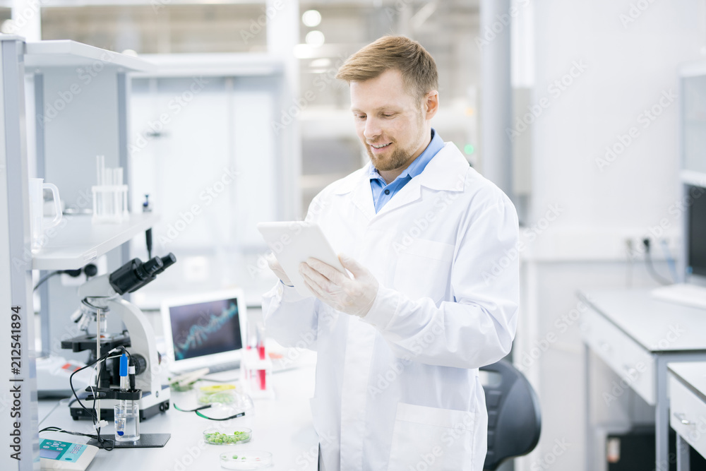 Waist up portrait of smiling young scientist wearing lab coat working on research using digital tablet, copy space Waist up portrait of smiling young scientist wearing lab coat working on research using digital tablet, copy space
