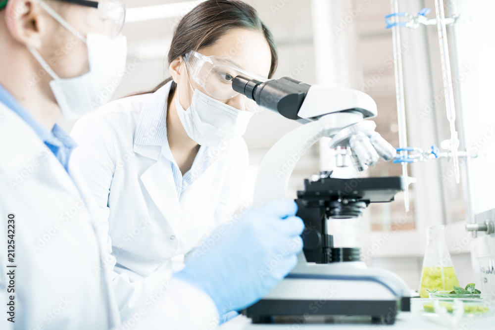 Portrait of two modern scientists working on food research studying liquids in beaker while sitting at table in laboratory and using microscope Portrait of two modern scientists working on food research studying liquids in beaker while sitting at table in laboratory and using microscope