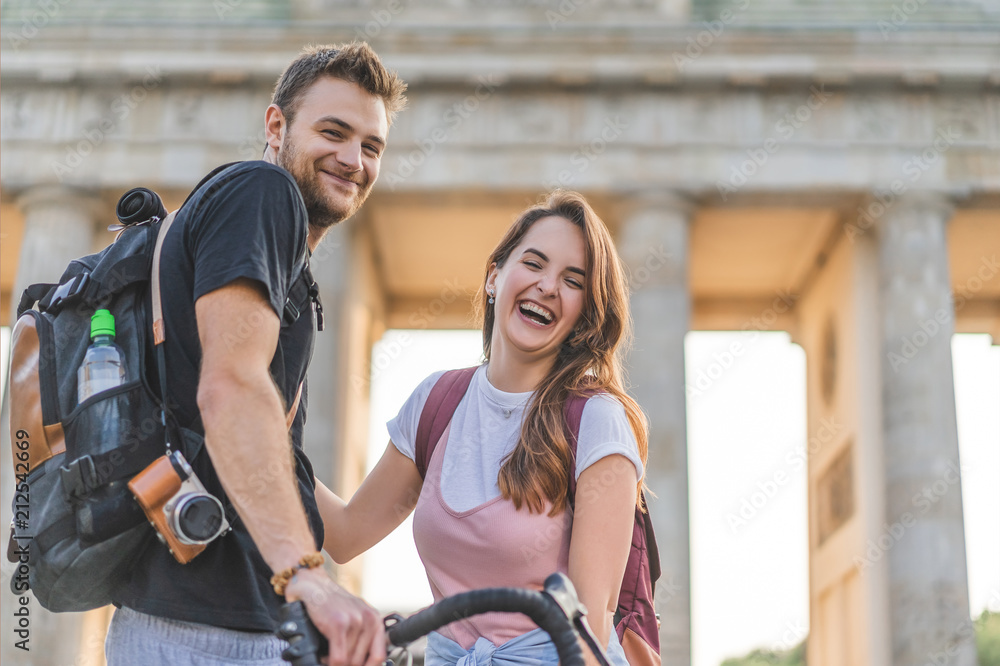 low angle view of happy couple of tourists with backpacks and bicycle in front of Brandenburg Gate, Berlin, Germany