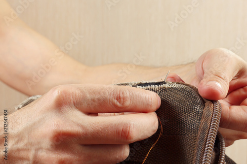 Photos Hands of tailor sew durable cloth bag with a needle close up