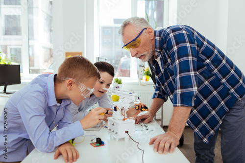 Science teacher. Serious smart man standing at the table while looking at his pupils working