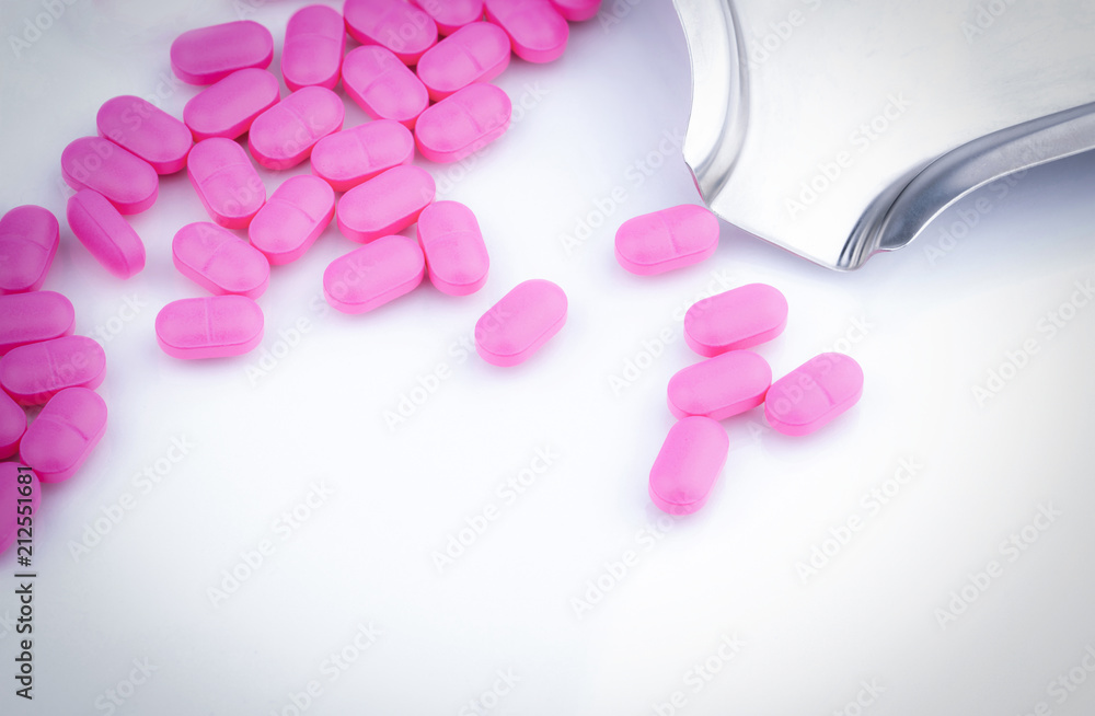 Pile of pink tablets pill on white background near stainless steel drug tray. Ibuprofen 400 mg. Painkiller medicine for headache, migraine, anti-inflammatory, high fever, arthritis, toothache. NSAIDs.