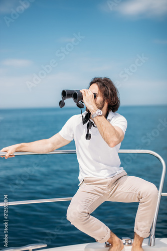 Caucasian Bearded Traveller Man looking through binoculars from the boat, adoring beauty and power of the Ocean photo