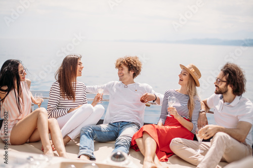 Two caucasian men invite three beautiful women to share pleasure yacht trip on the sea to islands, Young people laughing, enjoying amazing sea views