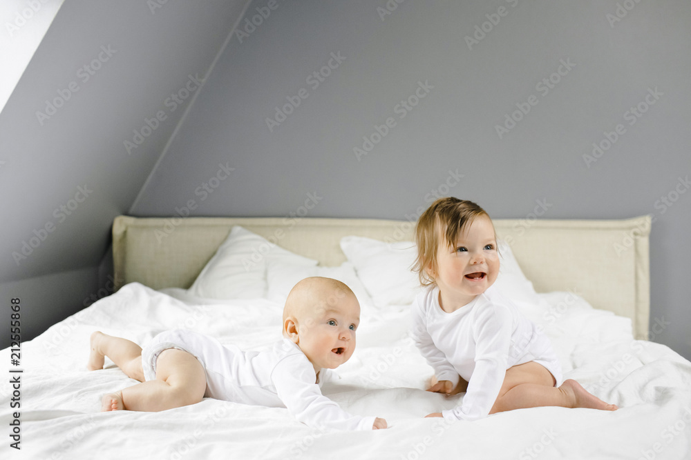 Two charming little babies lie on the white sheet and smile Two charming little babies lie on the white sheet and smile