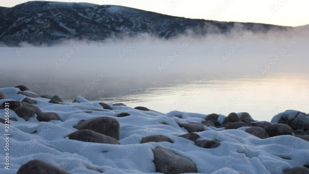 Snow covered rocks against a foggy lake background. Snow covered rocks against a foggy lake background.