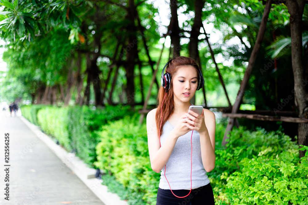Charming beautiful young woman is looking at smartphone for searching nice music in a park while beautiful Asia woman is jogging for exercise in the morning. Attractive beautiful girl has perfect body Charming beautiful young woman is looking at smartphone for searching nice music in a park while beautiful Asia woman is jogging for exercise in the morning. Attractive beautiful girl has perfect body