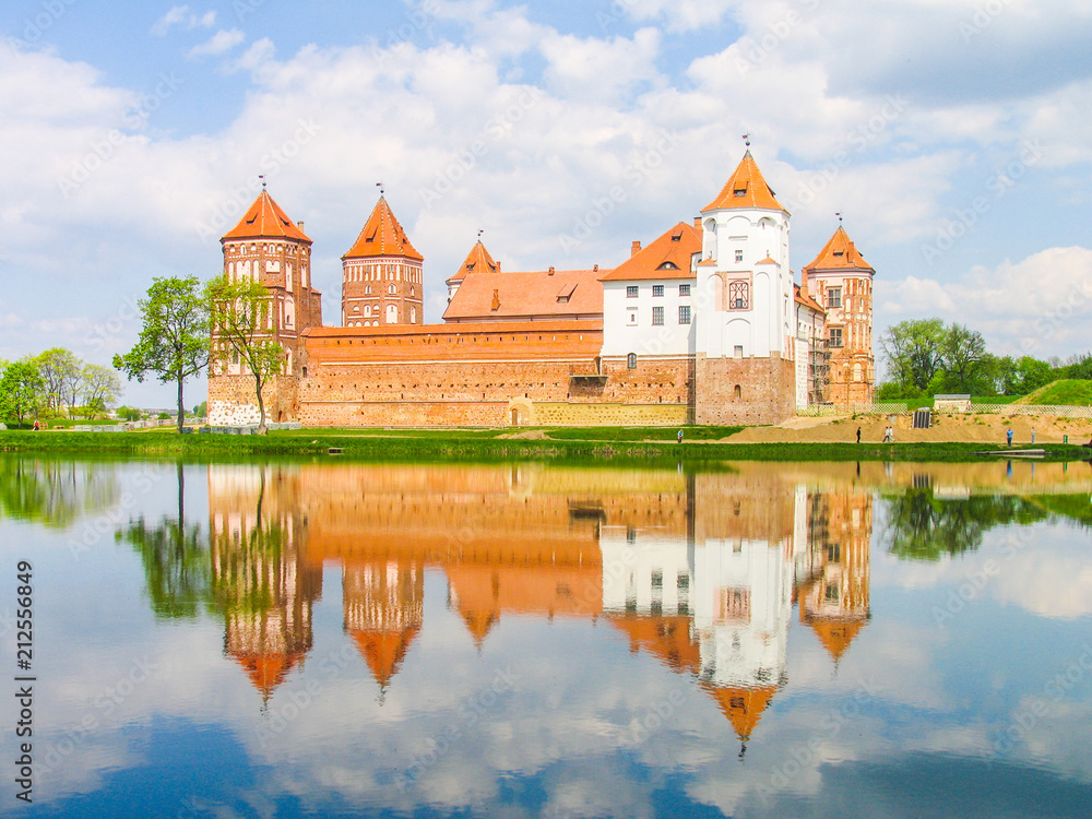 Mir, Belarus. Castle Complex Mir reflected in lake On Sunny Day with blue sky Background. Old medieval Towers and walls of traditional fort from unesco world heritage list Mir, Belarus. Castle Complex Mir reflected in lake On Sunny Day with blue sky Background. Old medieval Towers and walls of traditional fort from unesco world heritage list