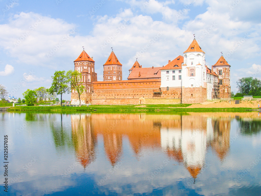 Mir, Belarus. Castle Complex Mir reflected in lake On Sunny Day with blue sky Background. Old medieval Towers and walls of traditional fort from unesco world heritage list
