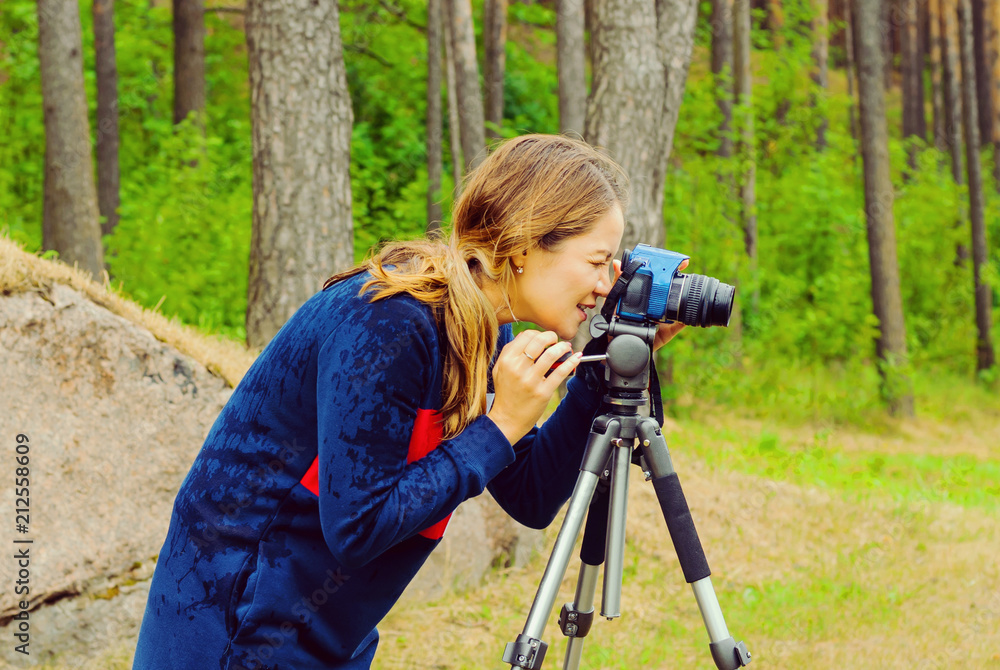 Freelance photographer shooting nature. Girl in the forest with a digital camera and tripod.