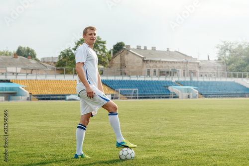 A football player stands on the field before the match and holds the ball with his foot. Determined to win the championship © oes