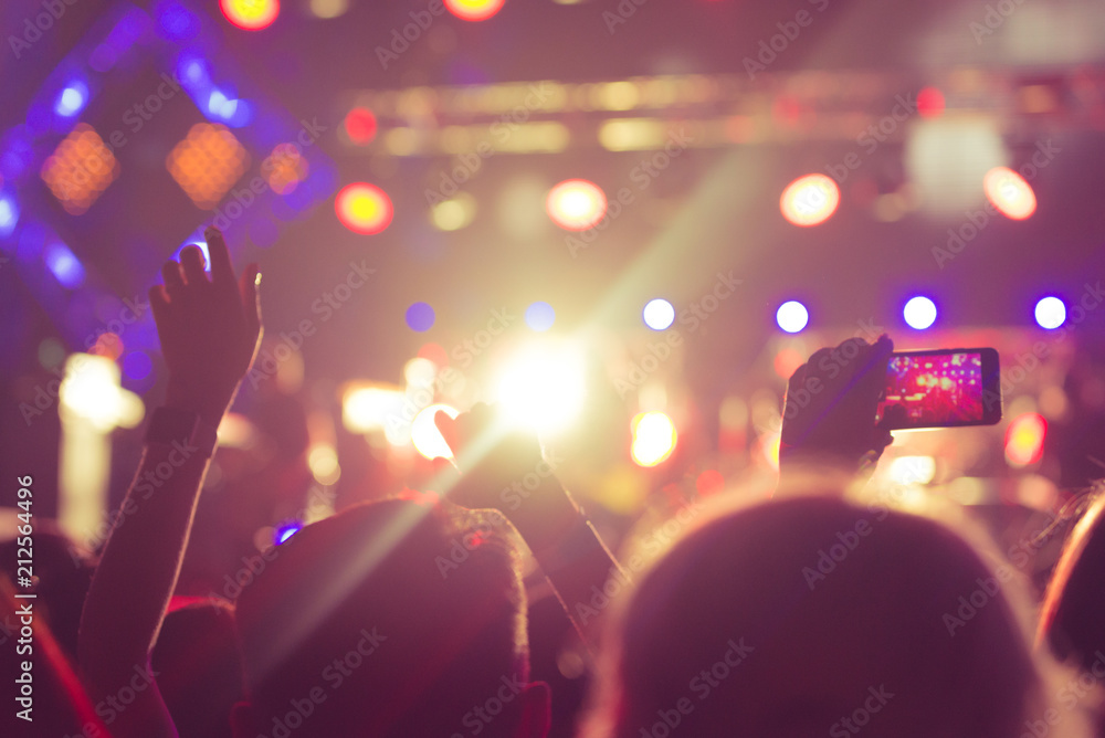 Audience with hands raised at a music festival and lights streaming down from above the stage. Soft focus, blurred movement.