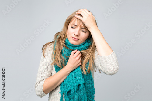 Beautiful young woman in knitted scarf suffering from headache standing against grey wall