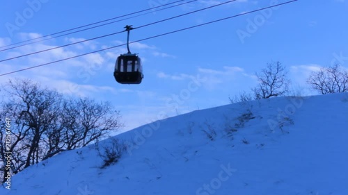 Cable car goes by one another against a blue sky background, with a close snow covered hill. photo