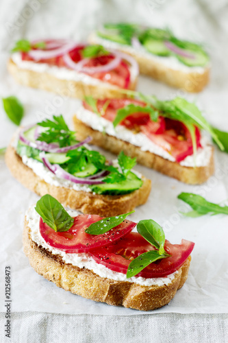 Bruschetta or sandwiches with tomatoes, cucumbers and cream cheese, decorated with greens.