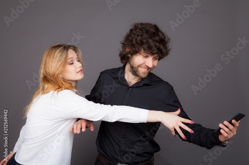 a young woman trying to take a phone from a man. Photo taken in studio on a gray background