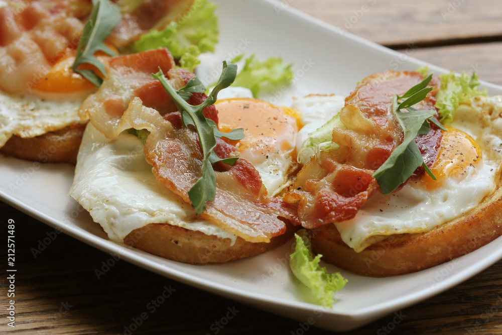 Bruschetta with rucola, chrispy bacon and poached egg served on white plate