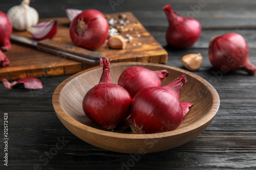 Plate with ripe red onions on wooden table