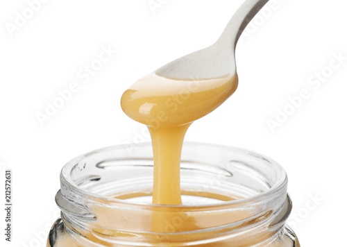 Honey dripping from spoon into jar on white background