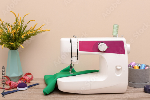 Modern sewing machine on table against light background photo