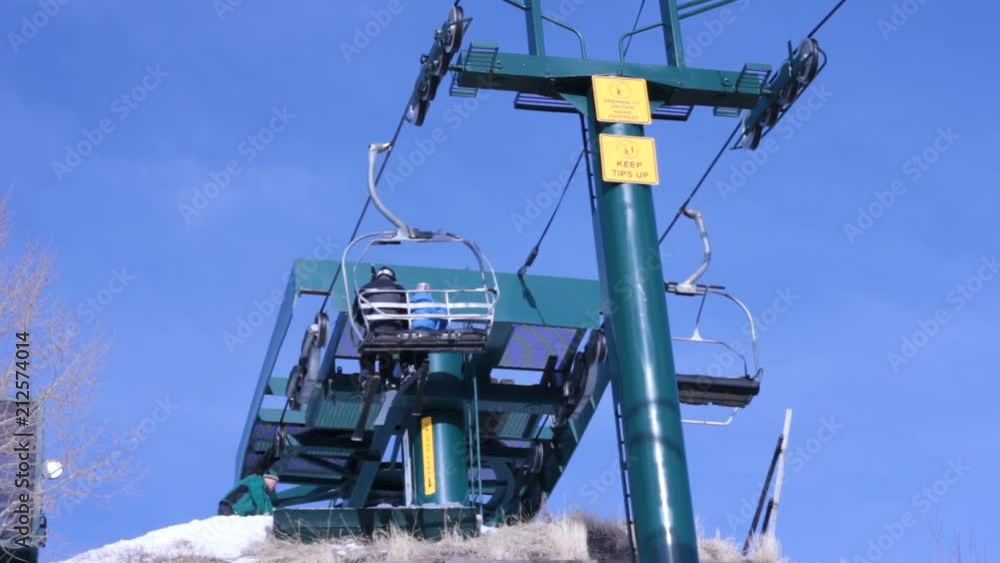 Skiers unload at the top of a hill. POV from under the lift looking up. a worker can be seen raking the snow. Skiers unload at the top of a hill. POV from under the lift looking up. a worker can be seen raking the snow.