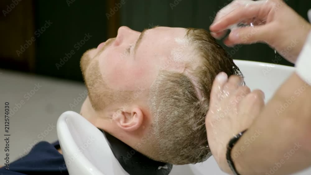 Preparing for the haircut. Male barber washing the head of the young man in barber's. 4K Preparing for the haircut. Male barber washing the head of the young man in barber's. 4K