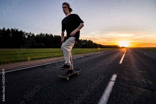 Skateboarder rides on empty road at the beautiful sunset