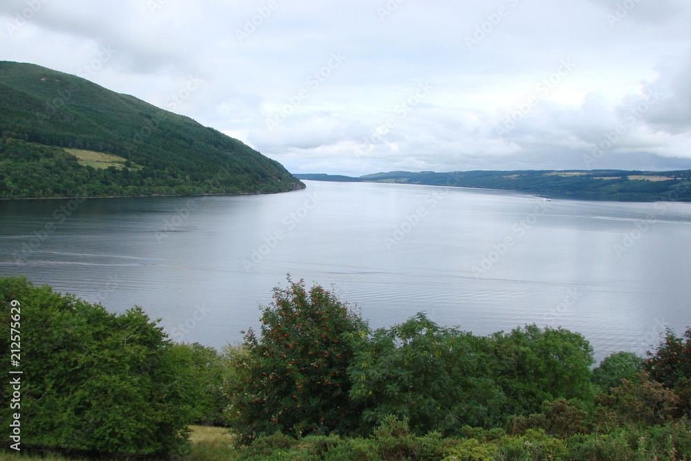 Landscape from the shore of the Scottish Fjords against the backdrop of mountain ranges and cloudy sky on the horizon.