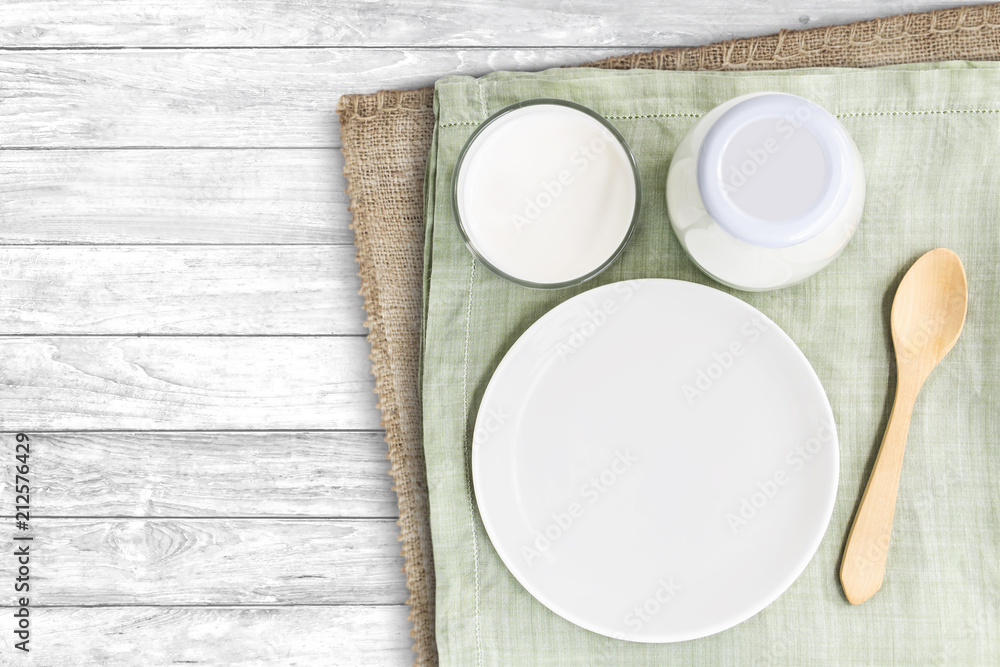A bottle of milk and glass of milk with blank dish and wooden spoon on green cloth and sackcloth isolated on wood background for food and healthy concept. with copy space for text. A bottle of milk and glass of milk with blank dish and wooden spoon on green cloth and sackcloth isolated on wood background for food and healthy concept. with copy space for text.